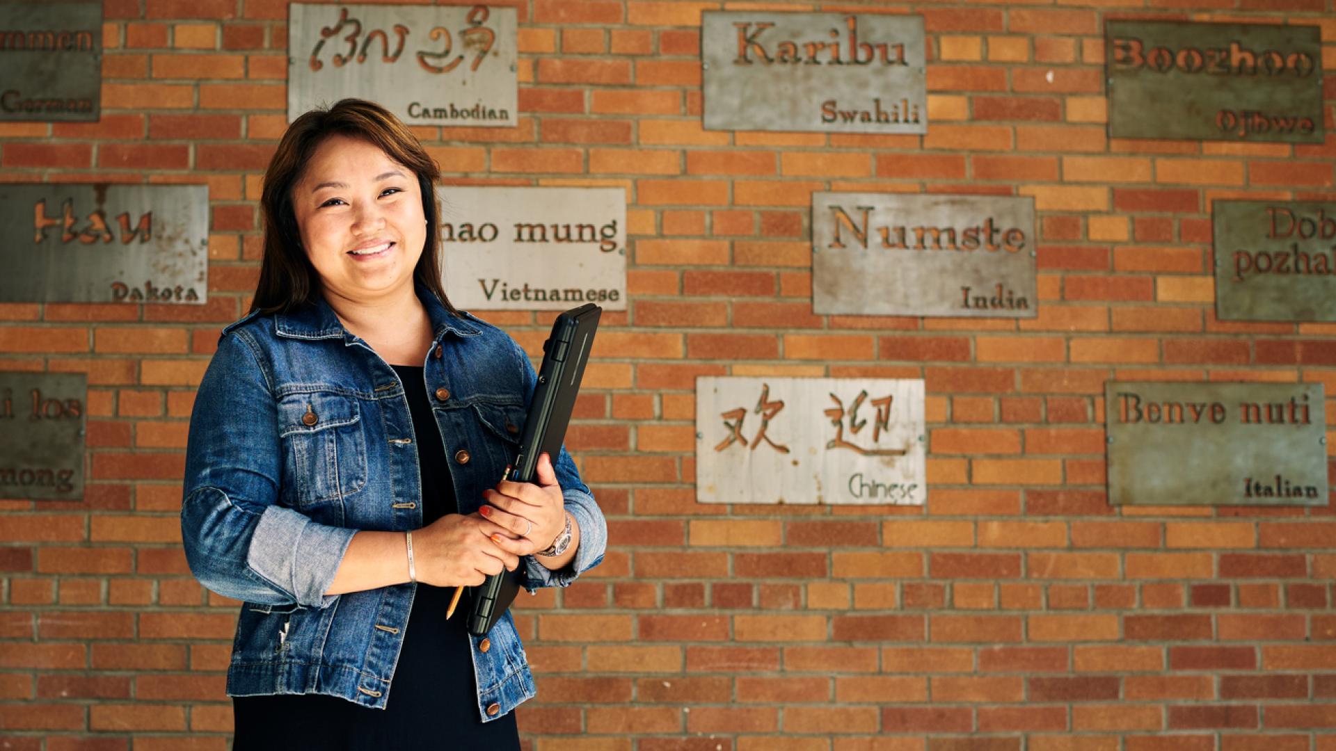 TESOL teacher with multi-language words on wall behind her
