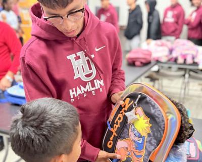 Men's soccer player showing backpack to a child. 